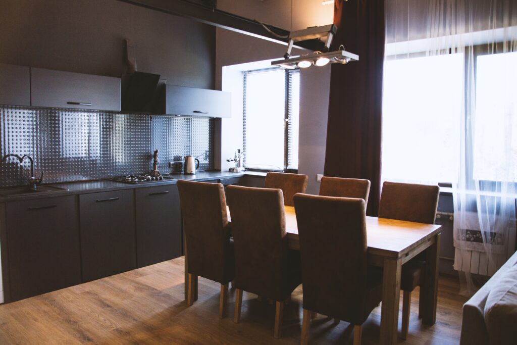 shot of a wooden table with wooden chairs near window curtains in a kitchen with black interior